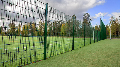 Palloilukenttä on aidattu vihreällä kolmilankaelementtiaidalla maalintaustaosissa elementtiaitaa on kororettu.