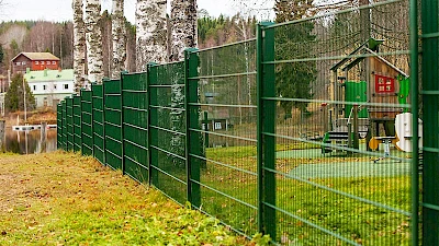Leikkipuisto on aidattu vihreällä elementtiaidalla.