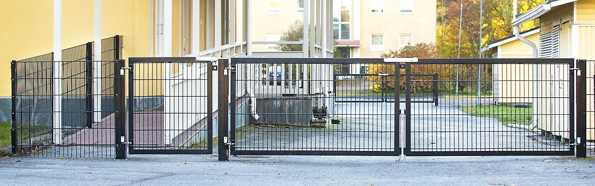 Rakennusten välistä piha-aluetta suojaa musta elementtiaita ja pihan molemmilla puolilla on saranoidut yhdistelmäportit, joissa on sekä ajoportti että käyntiportti.
