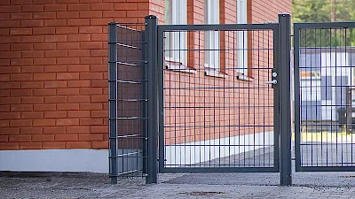 Rakennuksen seinään rajautuu tummanharmaa elementtiaitaus ja aidannurkkauksessa on abloy-lukittava käyntiportti jalankulkijoita varten.