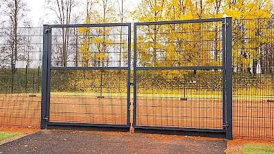 Tenniskenttäää ympäröivään mustaan elementtiaitaan on tehty korkea, saranoitu kaksilehtinen huoltoportti, josta pääsee kuljemaan ajoneuvoilla.