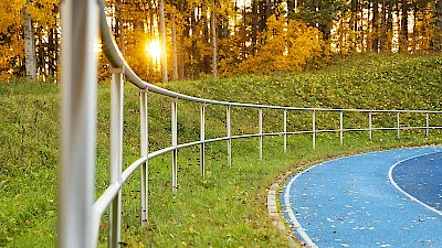 Ilta-aurinko paistaa kaartuvaan kaksijohteiseen alumiinikaiteeseen juoksuradan laidalla.